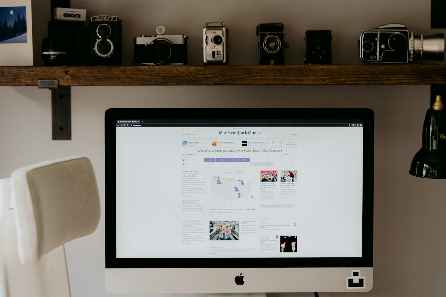 Vintage cameras displayed on a shelf above a computer monitor.